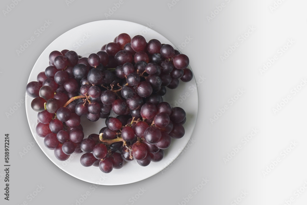 top view a bunch of purple grapes placed on a white dish on grey background, fruit, copy space top view a bunch of purple grapes placed on a white dish on grey background, fruit, copy space