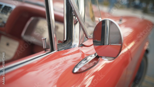 Details of red retro car on a blurred city background. Action. Close up of round rear view mirror of the old fashioned polished shiny red vehicle.