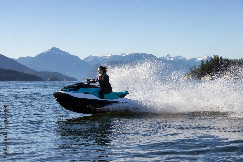 Fototapeta premium Adventurous Caucasian Woman on Sea-Doo riding in the Ocean. Lighthouse park in background. West Vancouver, British Columbia, Canada.