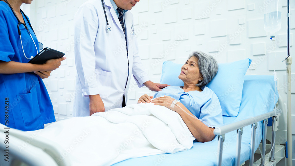 Obraz premium Specialist male doctor and his assistant came in to inquire about the symptoms of a female patient after receiving treatment. Female patient lying in bed responding to the doctor with a carefree face.