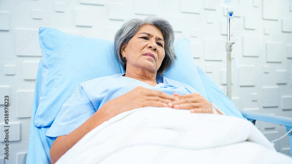 © P Stock - Elderly woman patient lying in bed receiving saline in the patient room feeling tired of an illness that is not getting better. Female patient lying in bed sigh and despair.