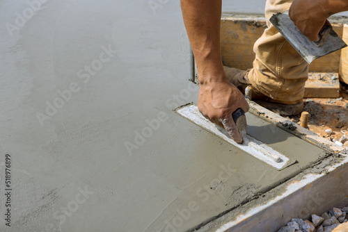 A masonry worker is smoothing the plastering concrete to cement floor while holding steel trowel in his hand