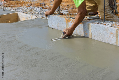 There is a masonry worker holding a steel trowel smoothing plastering concrete to a cement floor with a steel trowel