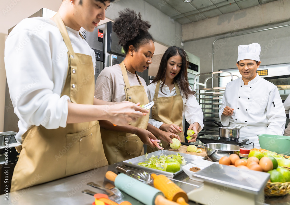 Cooking course , senior Asian male chef in cook uniform teaches young asian and african american people cooking class students to prepare, mix ingredients for pastry foods, fruit pies in restaurant . Cooking course , senior Asian male chef in cook uniform teaches young asian and african american people cooking class students to prepare, mix ingredients for pastry foods, fruit pies in restaurant .