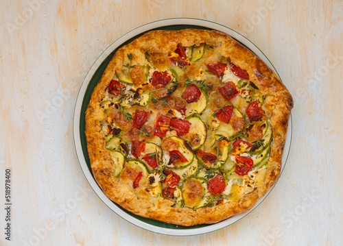 Open shortbread pie with zucchini, tomatoes, sweet peppers and mozzarella cheese on a ceramic plate on a light concrete background. Italian food.