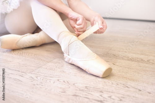 A ballerina sitting on the floor tying her ballet shoes