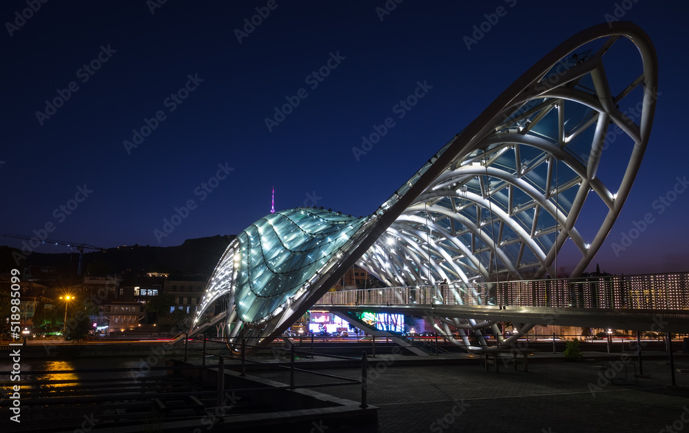 Obraz premium Bridge of Peace bow-shaped pedestrian bridge in Old Tbilisi town the Capital of Georgia. Twilight evening lights shot.