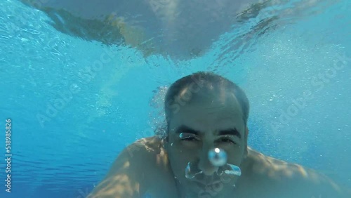 A man jumping into swimming pool and swimming in the underwater pool together with camera.  Above water and underwater view.