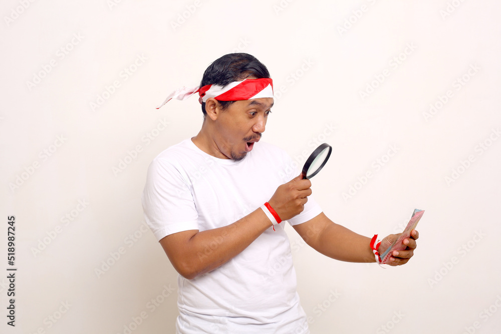 Asian man looking indonesian money through the magnifying glass. Indonesian independence day concept Asian man looking indonesian money through the magnifying glass. Indonesian independence day concept