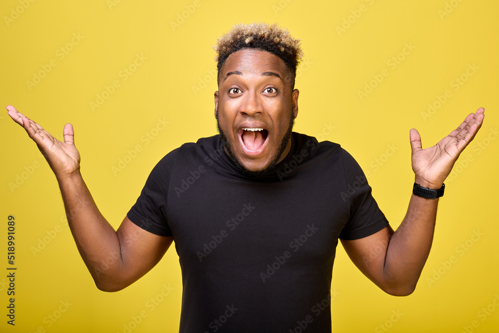 Surprised African-American, in a casual black T-shirt, isolated against a yellow background. Joyful young guy of pleasant appearance spread his arms to the sides. Keeping mouth open, spreading hands Surprised African-American, in a casual black T-shirt, isolated against a yellow background. Joyful young guy of pleasant appearance spread his arms to the sides. Keeping mouth open, spreading hands