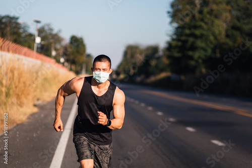 Athletic Asian man wearing face mask and running on the road during coronavirus outbreak. Muscle runner male with protective masks jogging on street and looking at camera. Air pollution problem