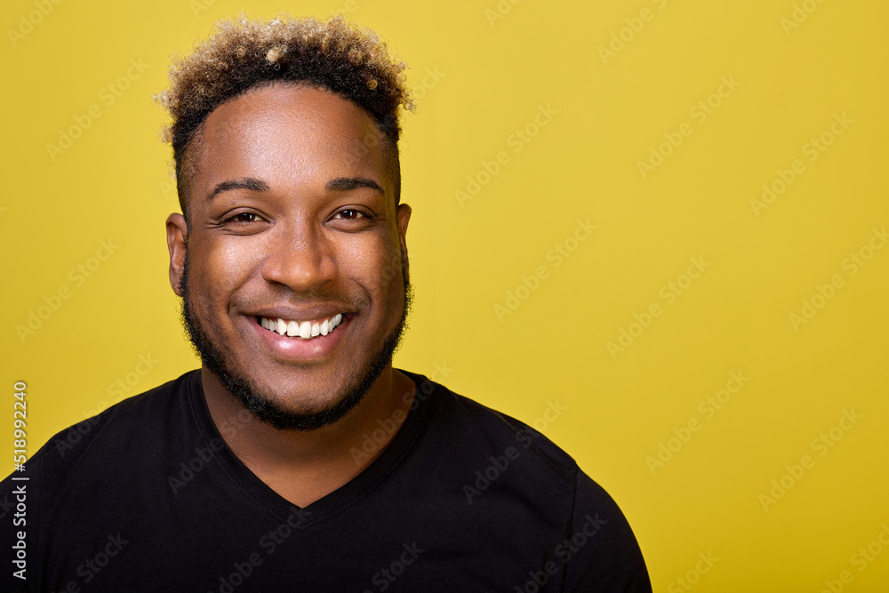 A young stylish black man in an everyday black T-shirt smiles against a yellow background at a close-up camera. Curly African-American shines with a snow-white smile after the dentist A young stylish black man in an everyday black T-shirt smiles against a yellow background at a close-up camera. Curly African-American shines with a snow-white smile after the dentist