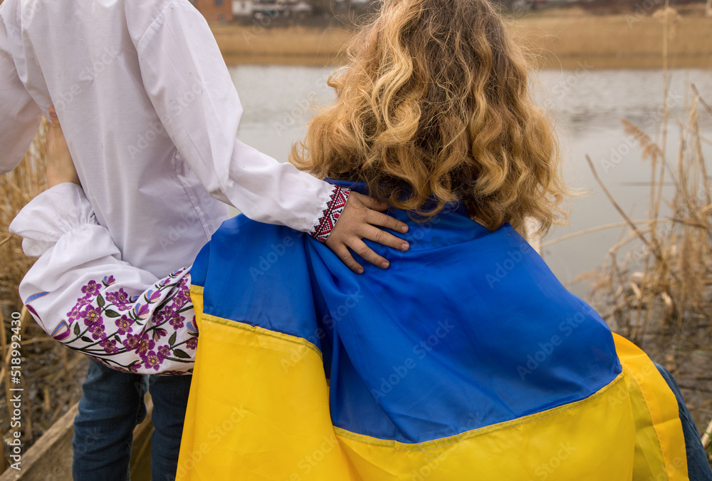 boy and woman dressed in traditional embroidered clothing with blue yellow flag. child's hand on shoulder of adult. concept of nation, patriotism, support. Stop war in Ukraine. Pride to be Ukrainian.