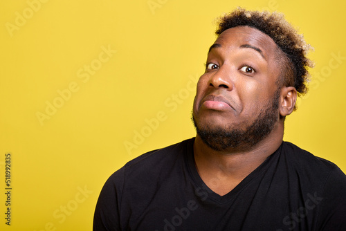 Young man in casual clothes looks questioningly at the photographer. A dark-skinned, handsome unshaven man with curly hair looks into the camera lens with a surprised look.  photo