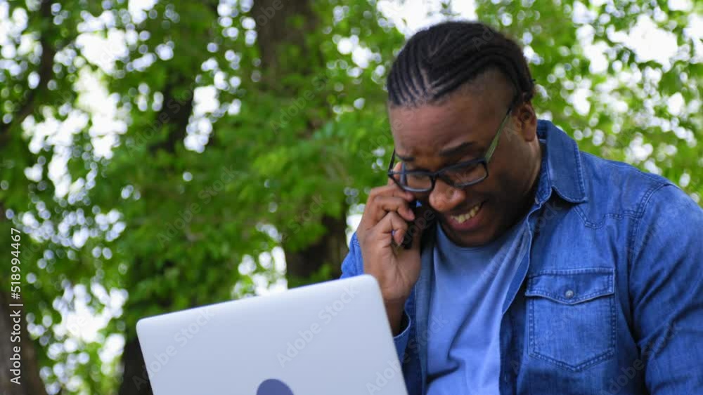 Handsome black man heard great news while talking on the phone while sitting in a park. Working in park with a laptop, an African entrepreneur received a very profitable offer. Emotional conversation Handsome black man heard great news while talking on the phone while sitting in a park. Working in park with a laptop, an African entrepreneur received a very profitable offer. Emotional conversation