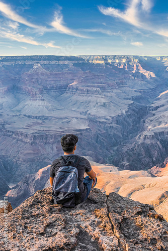 Young guy hiker sitting on the border of cliff gazing the Grand Canyon with copy space. 