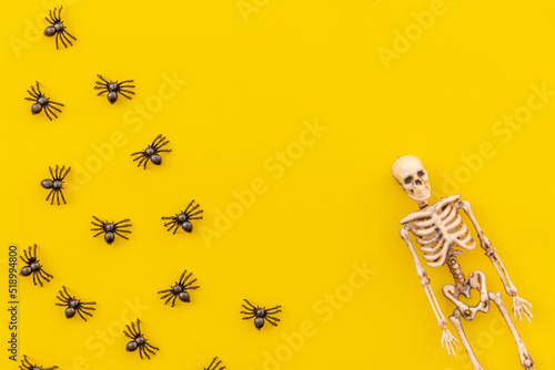 Halloween minimal decorations, composition with many black spiders and skeleton isolated on yellow background. Halloween celebration trick or treat concept. Flat lay top view copy space