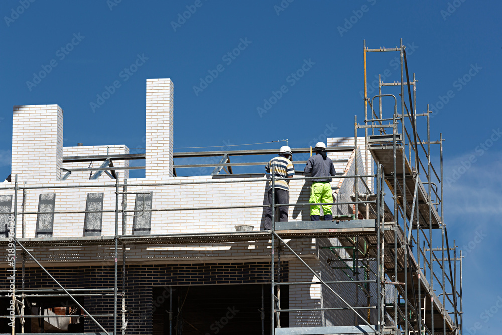Dos obreros trabajando en la construcción de una casa subidos en un andamio.
