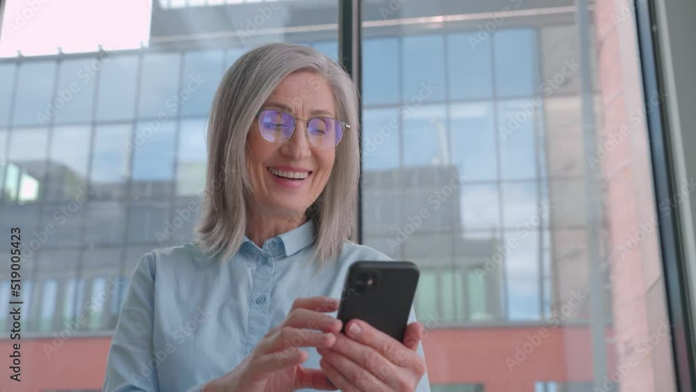 Middle age 60-s old senior businesswoman is using a smartphone in an office. Middle age 60-s old senior businesswoman is using a smartphone in an office.