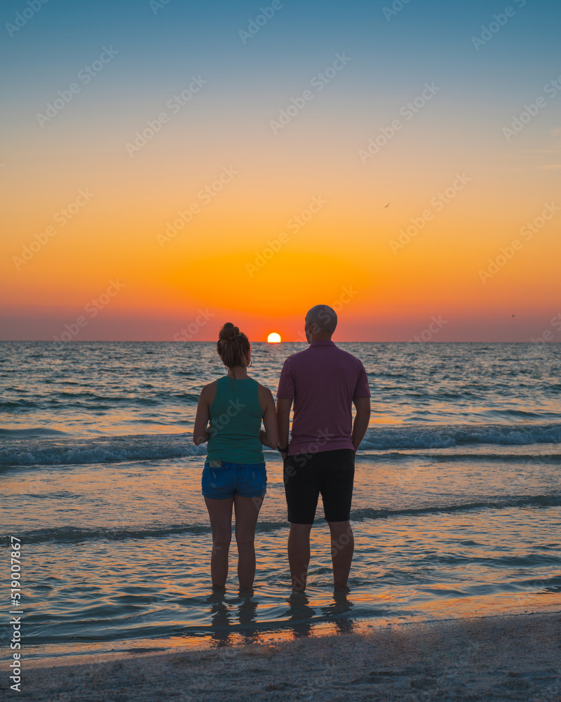 Ocean sunset. Couple man and woman on the beach. Family on summer vacation. Beautiful bright sunset. Silhouette of couple girl and boy.