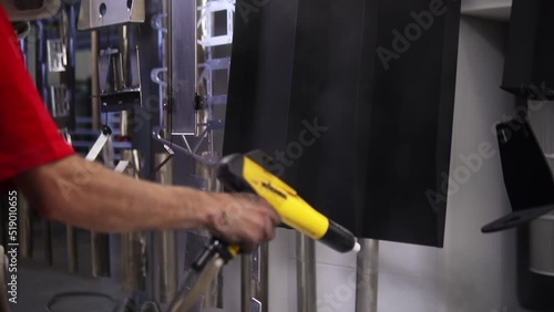 Powder coating of metal products. Employee in a protective mask with an aerosol pistol Kraskit metal parts with black color