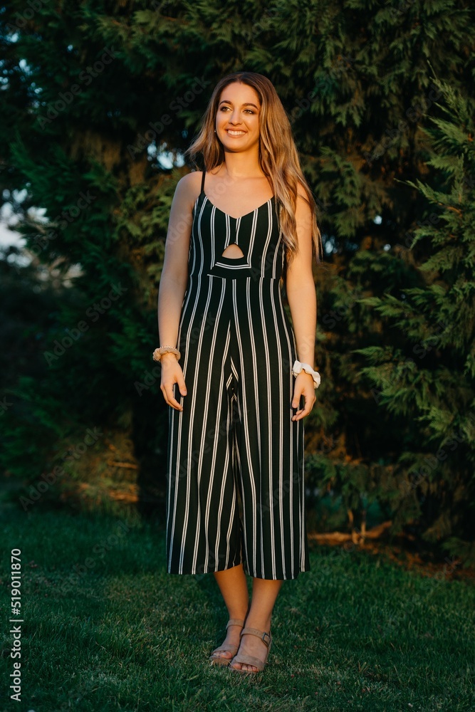 A full-length photo of a smiling girl who is posing with green bushes in the background at the sunset in Valencia.