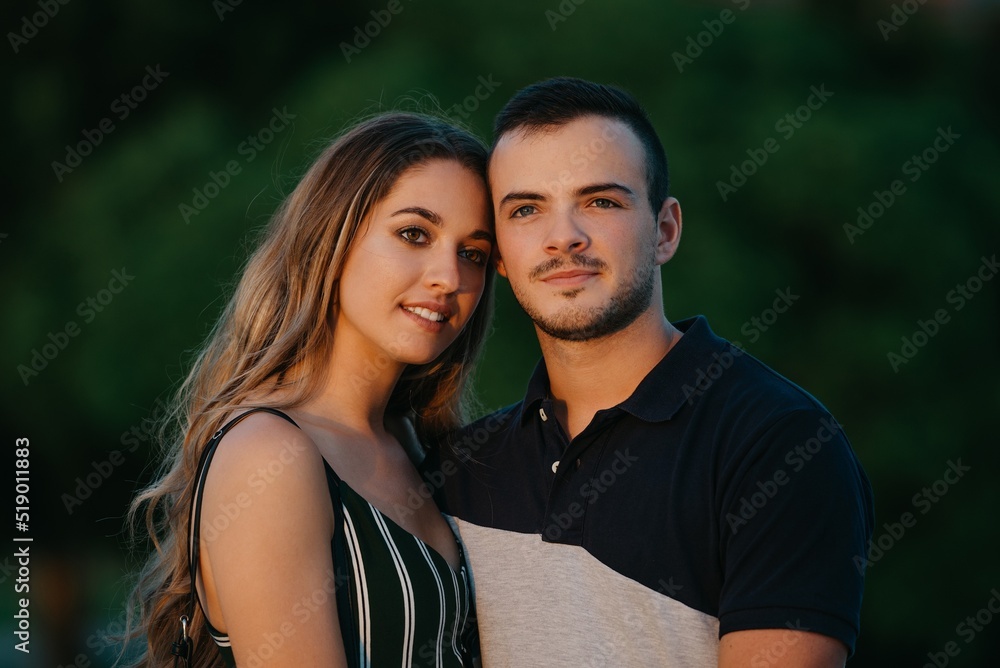 A couple of tourists are having fun with green bushes in the background on a date at the sunset in Valencia. A guy is hugging his girlfriend in the evening in Spain