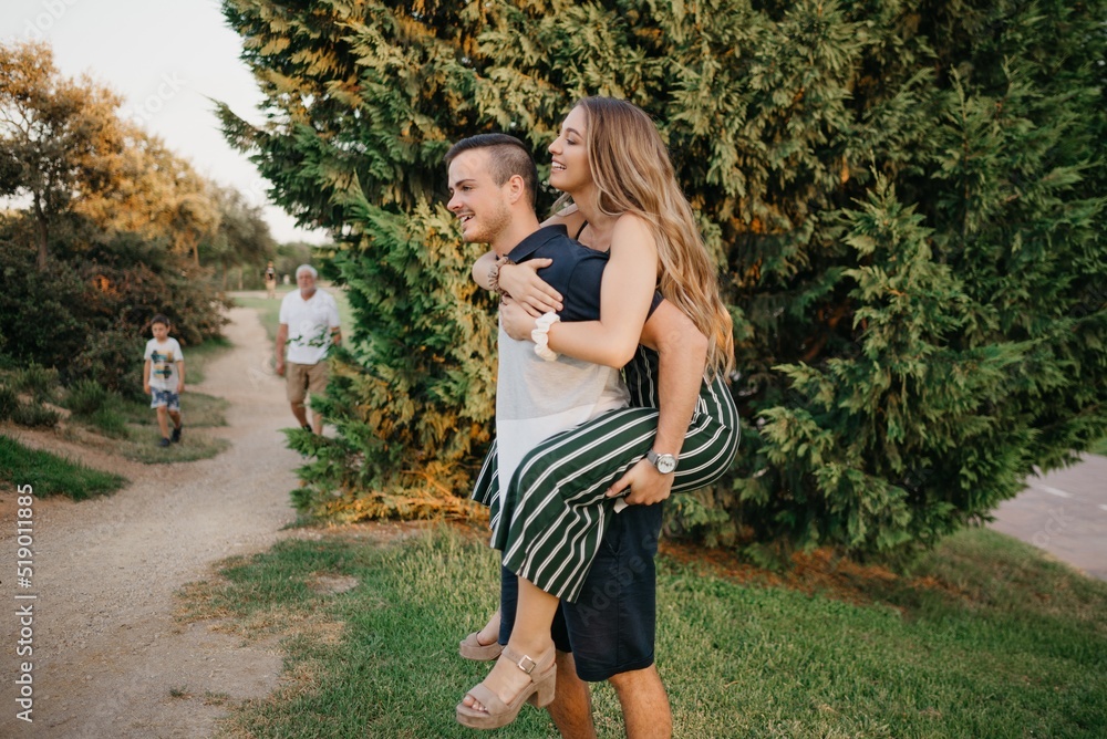 A smiling couple of tourists are having fun in the modern urban space on a date at sunset in Valencia. A girl is riding her boyfriend in the evening in Spain.