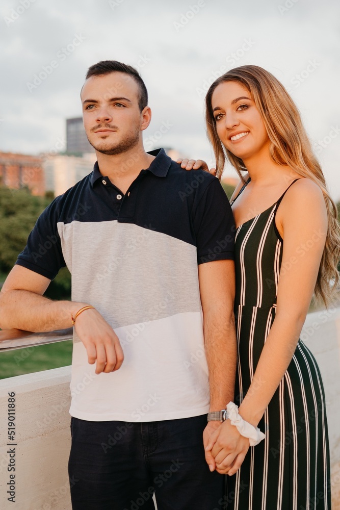 A couple of tourists are having fun with modern urban space in the background on a date at the sunset in Valencia. A girl is holding the hand of her boyfriend in the evening in Spain