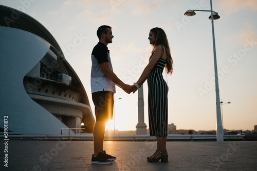 A couple of tourists who are having fun in the modern urban space at sunset in Valencia. A guy is holding hands with his girlfriend in the evening in Spain.