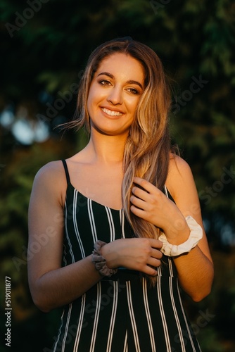 Obraz na płótnie A smiling girl is posing with green bushes in the background at the sunset in Valencia. w salonie