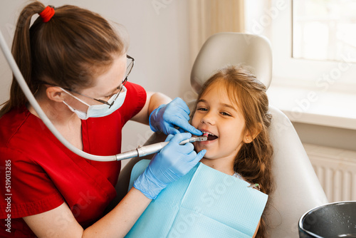 Pediatric girl dentist makes professional teeth cleaning in dentistry. Professional hygiene for teeth of child in dentistry. Pediatric dentist examines and consults kid patient in dentistry.