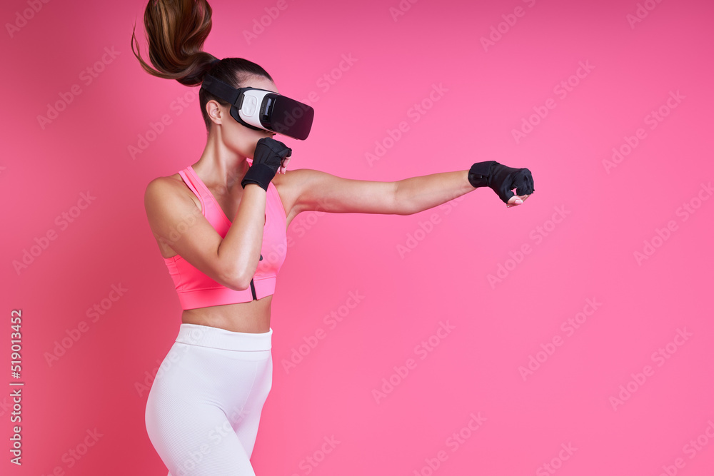 Concentrated young woman in virtual reality glasses boxing against pink background Concentrated young woman in virtual reality glasses boxing against pink background