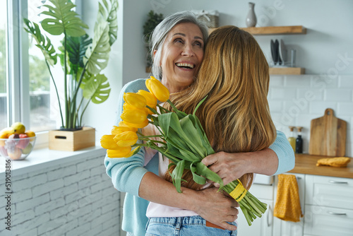 фотографія Happy senior woman embracing her daughter and holding a bunch of yellow tulips
