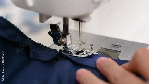 A woman sews a blue fabric on a sewing machine.