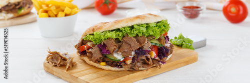 Döner Kebab Doner Kebap fast food meal in flatbread with fries on a kitchen board panorama