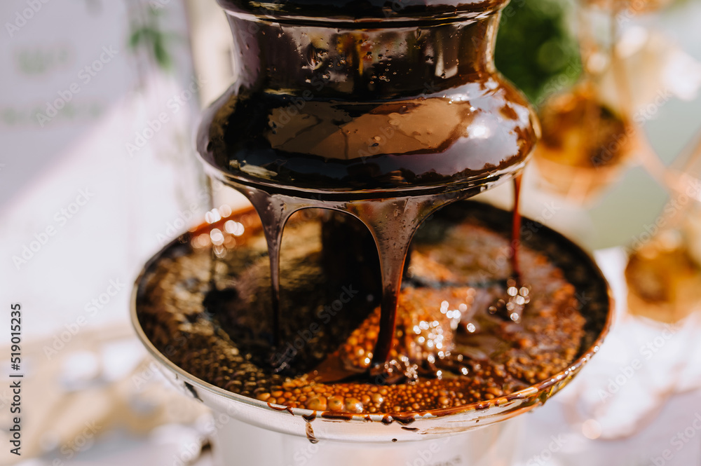Fototapeta premium Hot brown milk melted chocolate pours over the tiers of the fountain close-up. Food photography.