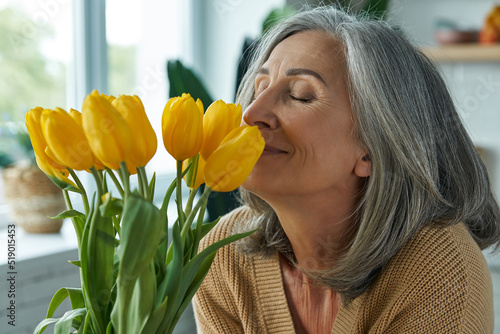 Happy senior woman smelling a bunch of yellow tulips while relaxing at home photo