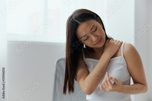 Suffering from shoulder dislocation neuralgia tanned beautiful young Asian woman touching painful shoulder at home interior living room. Injuries Poor health Illness concept. Cool offer Banner