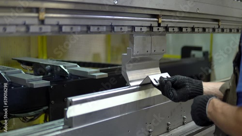 The employee hands are not bending the large parts of the metal on the bending machine, closeup. The CNC operator bending a metal product bends. The employee works at the metal factory.
