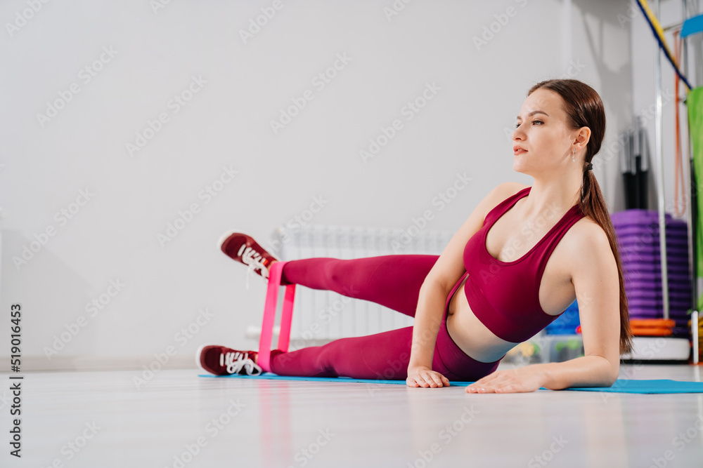woman in a tracksuit does leg exercises with gymnastic elastic bands on the side woman in a tracksuit does leg exercises with gymnastic elastic bands on the side