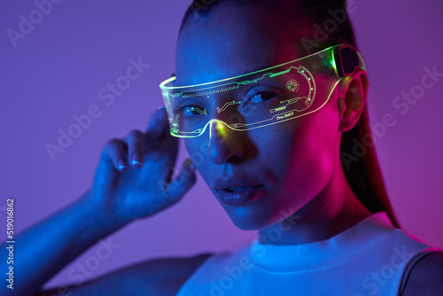 Beautiful young woman adjusting futuristic glasses against dark background