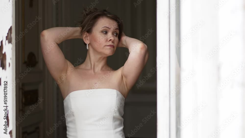 a gentle attractive woman in a white dress with bare shoulders at an open window a gentle attractive woman in a white dress with bare shoulders at an open window