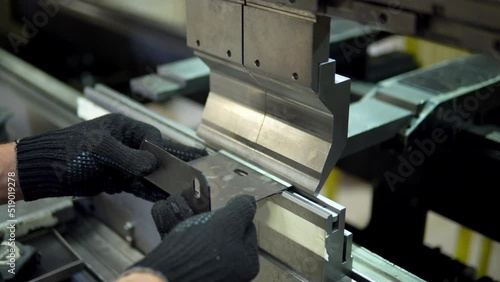 The employee hands are not bending the large parts of the metal on the bending machine, closeup. The CNC operator bending a metal product bends. The employee works at the metal factory.