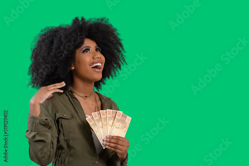 smiling woman holding money in her two hands, Brazilian money, isolated on green background	 photo