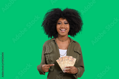 smiling woman holding money in her two hands, Brazilian money, isolated on green background	 photo