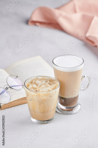 Ice coffee and coffee in a hight glass on the white table with a book and glasses 