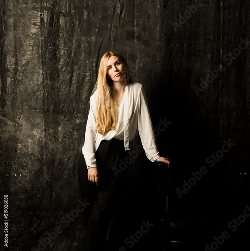 portrait of a beautiful blonde woman with long hair in a white blouse and black trousers on a gray isolated background.a charming girl posing on a dark background.