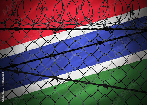 Gambia flag behind barbed wire and metal fence