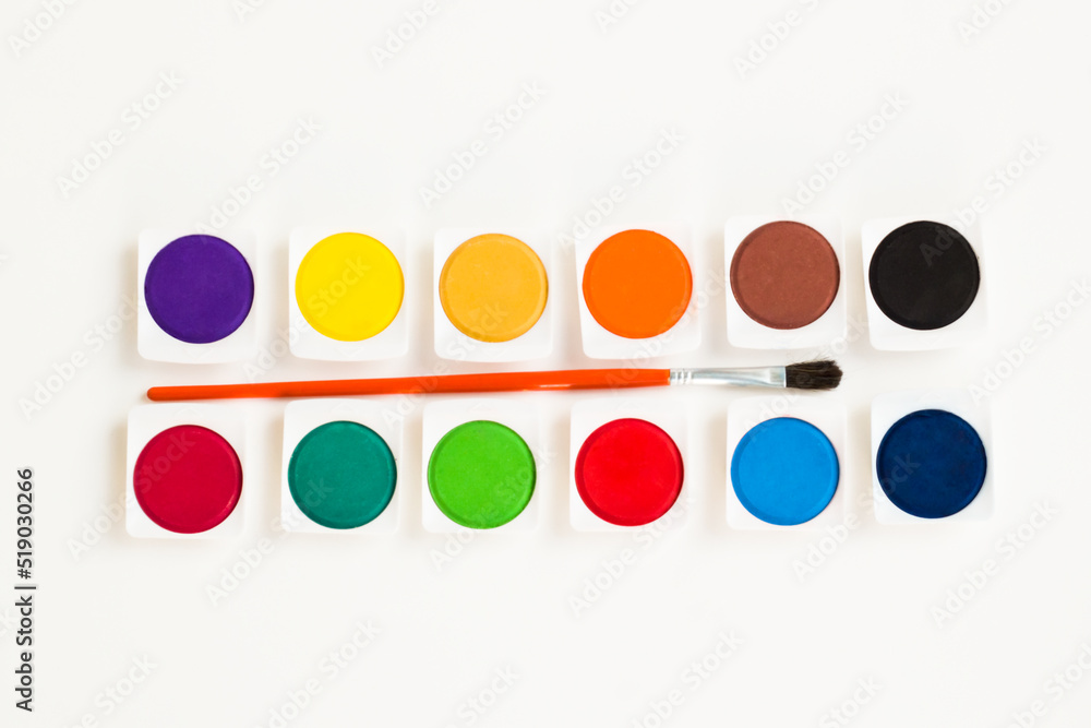 Set of twelve colorful watercolors with brush on a white surface